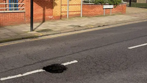 Jewel Miah A sink hole in the centre of a road