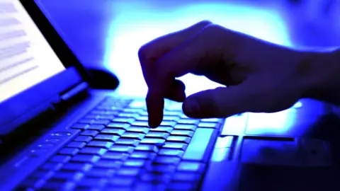 Getty Images A hand typing on a laptop in the dark.