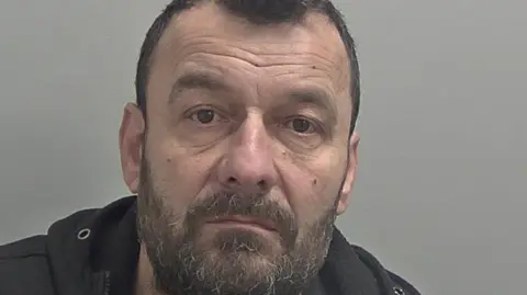 Police mugshot of Arian Varfaj who has a beard and short dark hair