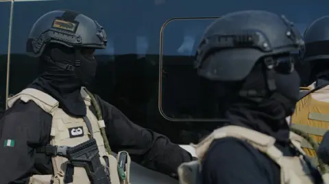 Two government forces personnel wearing all black and beige vests.