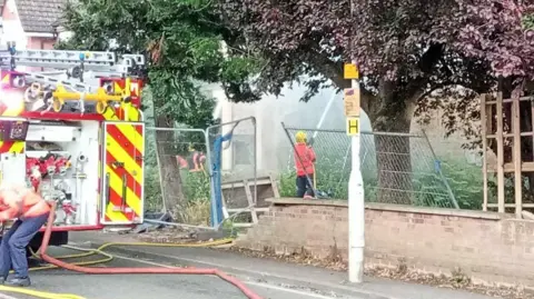 The fire service attending a house fire on London Road in Peterborough. The picture has the back of a fire engine in it and a firefighter is using a hose to tackle the blaze.