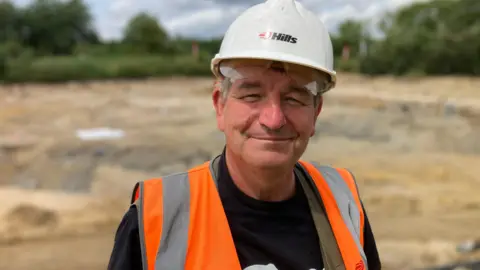 A man wearing a white hard hat and an orange high vis vest