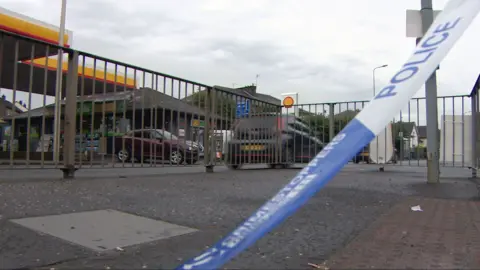 BBC A garage forecourt with a police blue and white banner draped across it.
