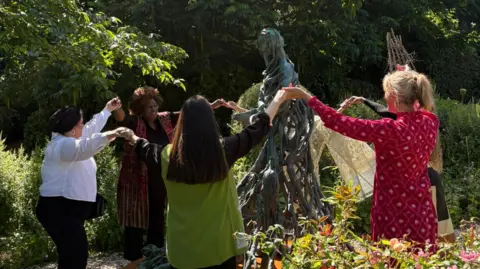 Sans Frontières Associates Survivors stood around the statue holding hands in the garden where it stands