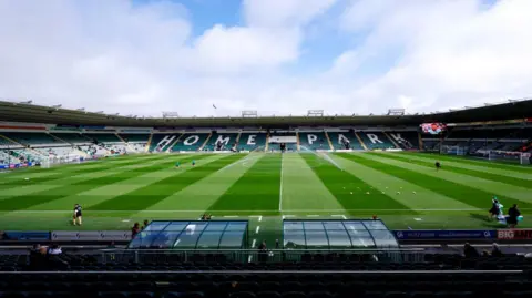 A picture taken from the side of home park stadium. It is a large stadium with grass in the middle 