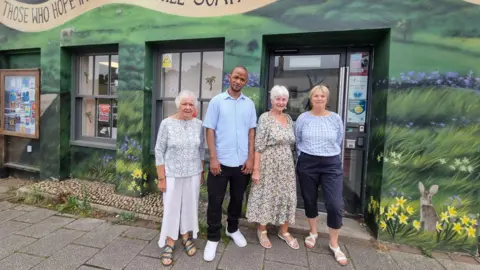 Alex Mayfield The team of volunteers at The Lord's Larder in Chard stand outside the food bank, the food bank is painted to look like a landscape in the spring