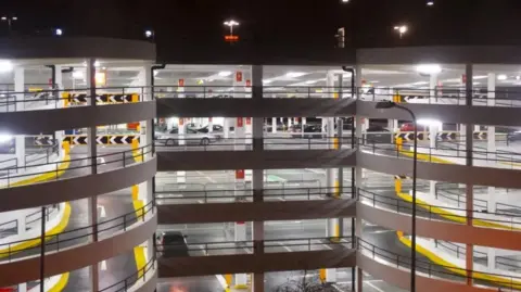 File photo of a concrete multi-storey car park with yellow kerbs around the spiral ramp on either side. A few cars are visible inside the well-built car park.