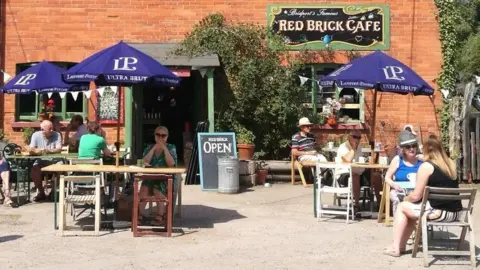 People sitting at tables in front of the Red Brick Cafe on a sunny day.