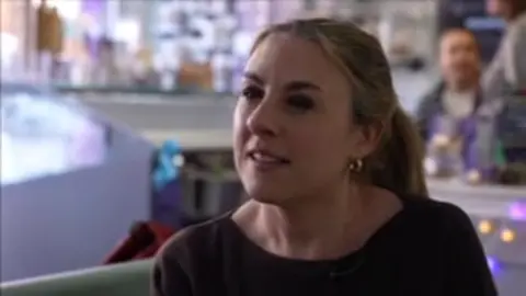 BBC Alex Hoskyn has light brown hair in a ponytail. She is wearing a dark jumper and is sitting in a cafe