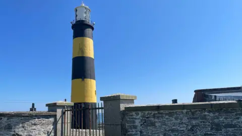 Getty Images St John’s Point Lighthouse in gorgeous County Down. Its strikingly tall tower is marked with vibrant bands of yellow and black. These vivid colours, which distinguish it from other lighthouses, are known as its daymark.