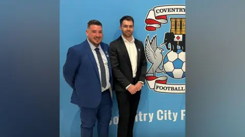 Matthew Loveitt Matthew Loveitt is pictured on the left in a blue suit jacket, blue trousers, black tie and white shirt smiling at the camera. Lewis Wale is on the right in a black suit jacket, black trousers and white shirt smiling at the camera. On a background behind them is the Coventry City emblem.