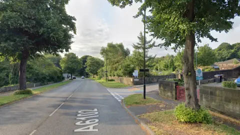 Google A suburban street with green trees and grass. A rainbow crossing is painted in one of the streets.