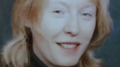 Kathleen Pitts smiling into camera in a family tribute photo. She has light hair at shoulder length and is wearing a dark jumper of which the top can be seen.