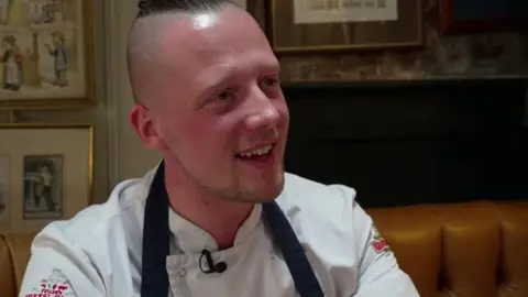 Luke Emmess in chefs whites sat at a table.