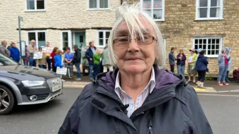 Barbara Lawrence stood in a road with campaigners behind her, holding placards