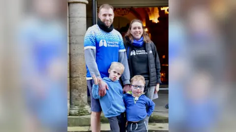 Charlie Waring A family stood together wearing blue and black shirts reading "Keep Me Breathing".