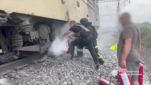 Emergency services use a fire extinguisher below a train
