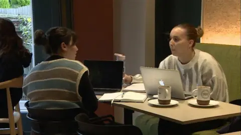 Two students work on laptops and notebooks at the Grounded cafe