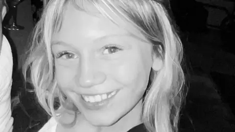 A close-up, black-and-white image of Sadie Reed. She is smiling as she looks directly into the camera. She has long blonde hair.