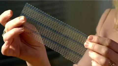 Close up picture of two hands holding a piece of mesh. It looks like a small straight net with holes and is white with horizontal blue stripes running across it