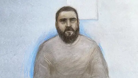 Court artist sketch of Mohammad Bashir. It shows man with short cropped black hair and a dark beard. He is wearing a light grey sweatshirt. 