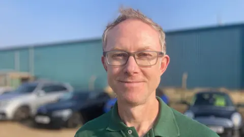 Luke Deal/BBC Ross Ovens of Scottish Power is pictured smiling to camera. He is wearing a green polo T-shirt with the Scottish Power logo embroidered on it. He has glasses and light coloured hair.