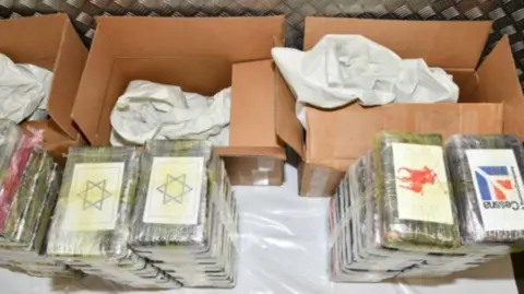 National Crime Agency Blocks of cocaine are wrapped in cellophane material, and have labels on them. The labels picture the star of david, the cessna logo and the ralph lauren logo. There are brown carboard boxes behind them