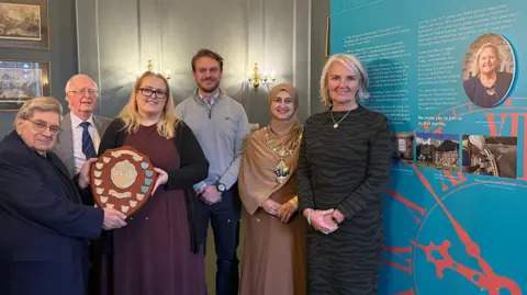 Rotherham Civic Society Rotherham Civic Society's Chair Brian King presents a shield to two of Dame Julie's children, Charlotte Kenny-Martin and Laurence Kenny (centre). Also pictured are Vice-Chair Dr David Sykes (second left), the Mayor of Rotherham Councillor Rukhsana Ismail, and Wentworth Woodouse Preservation Trust's CEO Sarah McLeod OBE (right, next to a photo of Dame Julie Kenny who died in February 2025)