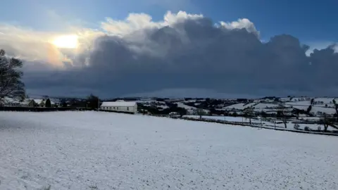 A field is covered in snow, as are hills in the background. a small church can be seen in the foothills of the sperrin mountains