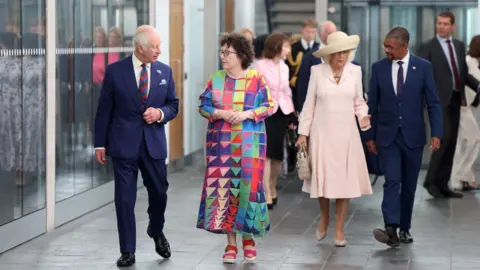 PA Media King Charles walking in the senedd foyer chatting with Elin Jones presiding officer, with Queen Camilla and First Minister Vaughan Gething walking behind them 