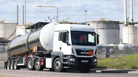 A white tanker truck enters the Navigator Terminal in Grays in April, with oil, gas and fuel storage units in the background on a cloudy day.
