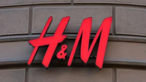 A red H&M sign is hung on a beige sandstone brick wall. 