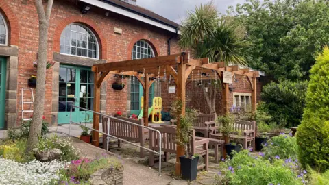 Sally Fairfax / BBC A picture of the garden. There are trees, shrubs, a patio and benches.