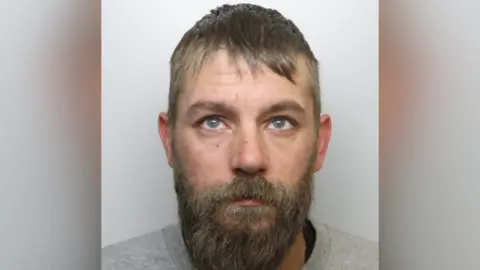 A white man with dark hair and a long beard
