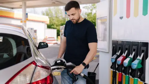 Getty Images Young man wearing a blue striped T-shirt filling a car with petrol