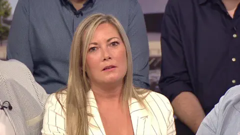 A woman with blonde hair and white-and-black striped blazer looks directly into the camera