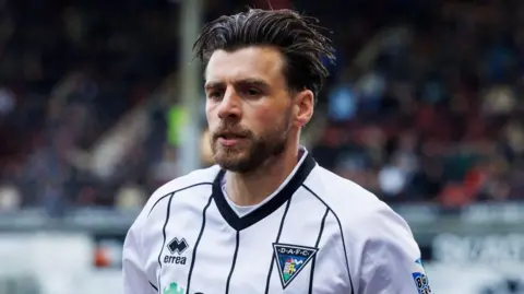 SNS Graham Carey playing football. He is wearing a black and white Dunfermline shirt.