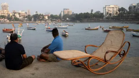 Hashim Badani A staged photo of a bentwood chair propped next to two men sitting near the Arabian Sea in Mumbai. 