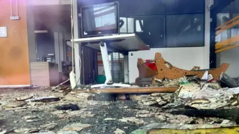 A photo of the library's interior, taken through the window, showing burnt debris on the ground