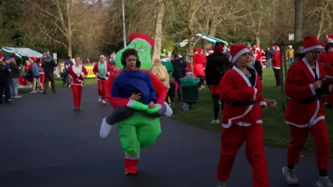 A young man heads towards the finishing line in a green The Grinch inflatable costume