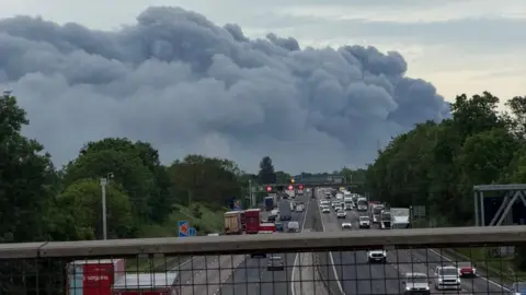 Andrew Lewis A huge plume of smoke in the distance, pictured from a bridge over a busy motorway.