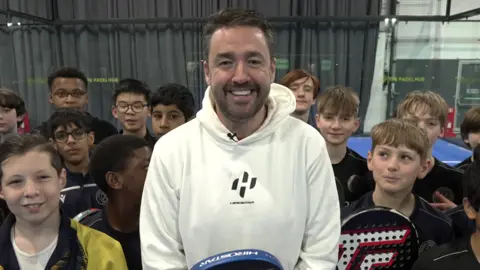 A picture of Jason Manford with children at the padel courts.
