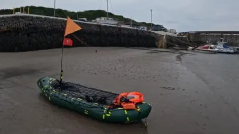 DAVID HIGSON A small inflatable boat with life jackets at the back and a Manx flag attached to a pole on the raft.