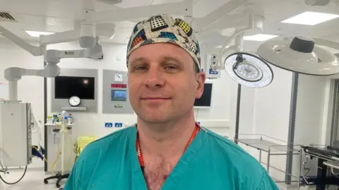 A man in green surgical scrubs and cap with daleks on it in an operating theatre