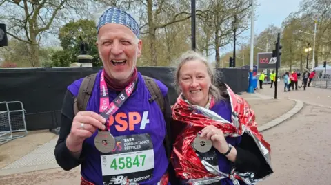 PSPA The pair posing on the Mall in running gear. They're smiling at the camera, and proudly showing off their medals.