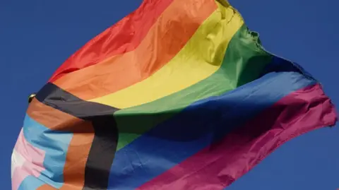 Joe Giddens/PA Wire Pride flag fluttering against blue sky background