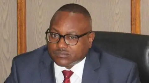 Minister Mulambo Haimbe in a suit seated in his office 
