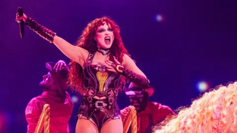 Getty Images Chappell Roan holding a microphone above her head while performing on stage wearing a corset 