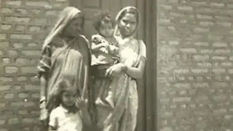 Sarita Paik A black and white photo of two women and children. Sarita Paik wearing a sari seen holding toddler Shailaja Paik in her arms