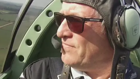 Pilot Trevor Bailey sitting in a cot-pit with headphones on, looking out the window to the left